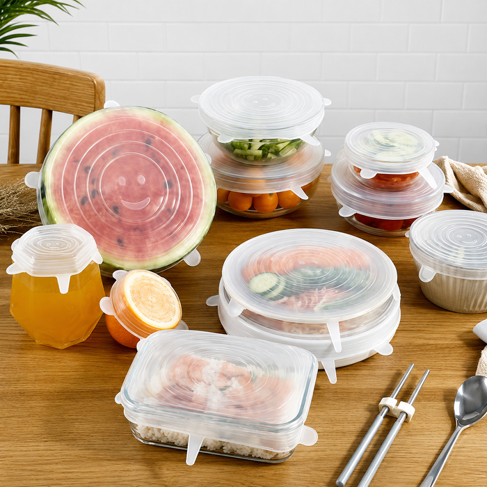 A set of reusable silicone stretch lids in multiple sizes, shown stretched over glass containers and around a watermelon, jar of honey, and fruit on a wooden table.